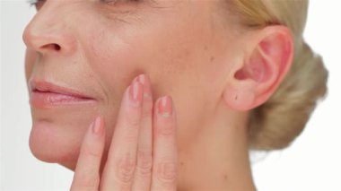 Zarif orta yaşlı bir kadının çarpıcı portresi kusursuz tenine dokunuyor el değmemiş beyaz bir arkaplana. Işıl ışıl cildi ve dingin ifadesi güzelliğin ve kendine bakmanın özünü somutlaştırıyor, cilt bakımının önemini gösteriyor.