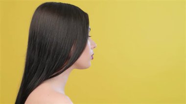 Çekici bir Asyalı kadın zarif bir şekilde başını kameraya çevirir ve güzel profilini canlı sarı bir arka plana karşı sergiler. Bu çekici yan bakış onun uzun, düz, esmer saçlarını ve büyüleyici özelliklerini ön plana çıkarıyor.