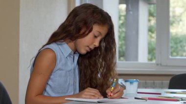 Çekici bir genç kız, okulda sanat projesi üzerinde çalışırken yaratıcılığı hızla akan mesafeye dikkatle bakar. Renkli sanat malzemeleriyle çevrili, çocukluk hayalinin ruhunu ve öğrenme sevincini somutlaştırıyor.