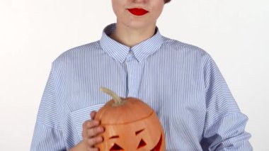 Güzel oyulmuş Cadılar Bayramı balkabağını tutan kırmızı rujlu neşeli bir kadın şenlik ruhunu sergiliyor. Bu canlı görüntü, güz kutlamalarının özünü yansıtıyor, geleneği neşeli cazibeyle harmanlıyor.