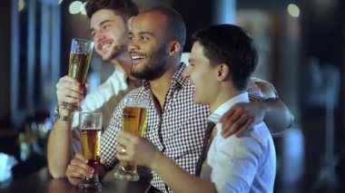 Üç neşeli arkadaş, bir siyah adam ve iki beyaz adam, kutlama için bira bardaklarını kaldırıyorlar, TV 'deki heyecanlı futbol maçının keyfini çıkarıyorlar. Barın hareketli atmosferi kahkahalarla ve arkadaşlıkla doludur.