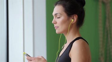 Işıl ışıl genç bir kadın içeride yoga yapıyor, kulaklıklarıyla müzik dinlerken kameraya parlak bir şekilde gülümsüyor. Bu canlı sahne, spor ve sükunetin özünü yakalıyor, ince vücudunu, parlak siyah bir elbiseyle,