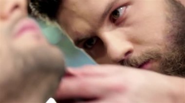 Şık bir berber dükkanında, yetenekli bir erkek kuaför, müşterisinin sakalını tımar etme, hassasiyet ve sanatını sergileme üzerine yoğunlaşır. Atmosfer hareketli ve şık, modern dekorlar modern erkekler için tımar deneyimini geliştiriyor.