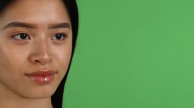Canlı bir kayma sahnesi, parlak gülümseyen genç bir Asyalı kadını yakalar, özgüveni parlak yeşil renkli arka planda parlar. Bu büyüleyici görüntü güzelliği ve canlılığı somutlaştırıyor, kusursuz cildini ve oyuncu cazibesini sergiliyor.