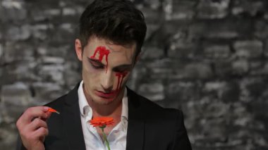 Parlak siyah bir takım elbiseyle süslenmiş erkek bir vampir, kan lekeli bir çiçeğe bakarken kaygı verici bir şekilde kara tuğla bir duvara bakıyor. Bu ürpertici sahne, Cadılar Bayramı 'nın özünü yakalıyor. Gizem ve büyüyü gotik bir korkuyla harmanlıyor.