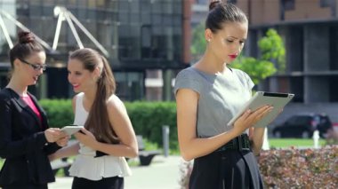 Dengeli genç bir iş kadını, ışıl ışıl gülümsemeden önce tabletine odaklanmış modern bir ofisin önünde duruyor. Etrafı profesyonellerle çevrili, şık giyimi ve kendine güveni kentin hareketli başarısını ve hırsını somutlaştırıyor.