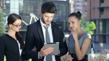 Üç dinamik iş ortağı, kendine güvenen bir adam ve iki şık kadın, heyecan verici haberler aldıklarında yüzleri neşeyle parlayan bir tabletin etrafında toplanıyorlar. Modern bir kentsel zemin üzerine kurulmuş bu ifadeler başarı ve işbirliği yayıyor.