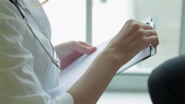 Şefkatli bir doktor, boynunda steteskopla, hastasını dikkatle dinler, her detayı yakalar. Huzurlu klinik atmosferi, özenle reçete yazarken, özenli bir bakım ve