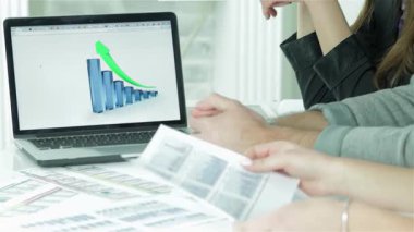 Kendine güvenen bir işadamı, canlı satış büyüme grafiklerini analiz eden meslektaşlarıyla çevrili olarak dizüstü bilgisayarına stratejik bir iş planı yazarken gülümsüyor. Atmosfer işbirliği ve coşkuyla dolu, modern bir ofis ortamı sergiliyor.