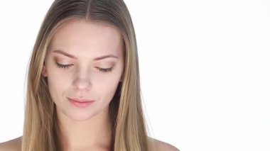 Çekici, genç, sarışın bir kadın taze, temiz bir yüzle nazikçe boynuna dokunuyor, saf, beyaz bir arka plana özgüven ve zarafet yayıyor. Bu büyüleyici portre onun kusursuz cildini ve büyüleyici gülümsemesini ön plana çıkarıyor.