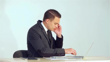Gösterişli bir takım elbise giymiş kararlı genç bir işadamı dizüstü bilgisayarındaki verileri özenle analiz ederken bir not defterine not alıyor ve bir telefon görüşmesine katılıyor. Bu dinamik sahne modern iş hayatının özünü yansıtıyor.