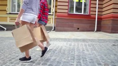 İki modaya uygun kadın büyüleyici bir kaldırım taşı caddesinde ellerinde alışveriş çantalarıyla geziyorlar. Canlı kıyafetleri ve neşeli ifadeleri mutluluk saçıyor, şehirde başarılı bir alışveriş çılgınlığının heyecanını somutlaştırıyor.