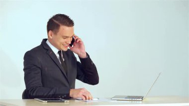 Sivri takım elbiseli neşeli genç bir işadamı, özenle bilgisayarına veri girerken bir telefon görüşmesi yapıyor. Dostane tavrı profesyonelliği ve yaklaşılabilirliği yayarak üretkenliğin dinamik atmosferini yaratıyor.