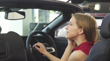 Çekici genç bir kadın saçlarını aynada düzeltirken zevkten dört köşe oluyor. Üstü açık arabasında oturuyor. Bu canlı sahne, yeni sahipliğin heyecanını yakalıyor. Açık yolların özgürlüğünü kucaklarken heyecanını gösteriyor.