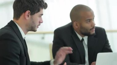 İki gülümseyen iş adamı, biri siyah saçlı, diğeri de kafası tıraşlı, şık bir konferans masasında stratejileri tartışıyorlar. Özgüvenli ifadeleri ve profesyonel kıyafetleri, canlı bir işbirliği atmosferini yansıtıyor.