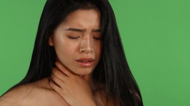 Göz kamaştırıcı genç bir Asyalı kadın, hafifçe öksürürken boğazına hafifçe dokunarak, gözleri yorgunluktan kapalıyken, iyi görünmüyor. Bu dokunaklı portre hastalığın özünü yansıtıyor, empati ve sağlığıyla ilgili endişeleri çağrıştırıyor.