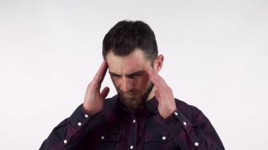 Koyu renk ekose gömlekli sakallı genç bir adam şiddetli bir baş ağrısıyla savaşırken şakaklarını ovuyor. Bu dokunaklı görüntü yoğun acıyla başa çıkma mücadelesini yakalıyor, empati uyandırıyor ve rahatlama ihtiyacını vurguluyor.