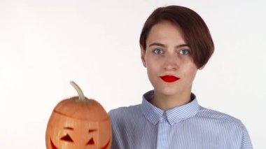 Çarpıcı kırmızı dudakları olan genç bir kadın elinde tuhaf oyulmuş bir Cadılar Bayramı balkabağı tutarken tamamen şok olmuş görünüyor. İfade dolu yüzü, mevsimin neşeli ruhunu yansıtıyor. Sonbaharın keyifli bir kutlamasında eğlence ve korkuyu harmanlıyor.