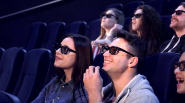 Üç boyutlu gözlük takan genç yetişkinlerden oluşan canlı bir grup, karanlık bir tiyatroda heyecan verici bir film sahnesinde kahkahalara boğuldu. Patlamış mısır ve gülümsemeleri paylaşıp unutulmaz anılar yarattıklarında atmosfer heyecanla dolup taşıyor.