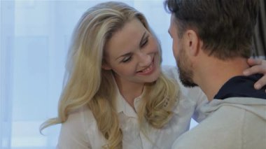 Çekici sarışın bir kadın kocasına sevgiyle sarılıyor. Yüzleri sıcacık bir dairede sıcaklık ve şefkat saçıyor. Yumuşak ışık, perdelerin arasından süzülür. Samimi ilişkilerini vurgular. Nazikçe boynunu okşar.