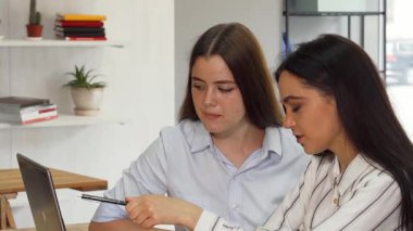 Dizüstü bilgisayar üzerinde çalışırken, yaratıcılık ve takım çalışması yayarak canlı bir tartışmaya giren iki genç kadın tasarımcının dinamik bir sahnesi. Şık kıyafetleri ve odaklanmış ifadeleri yenilik ve işbirliğinin canlı atmosferini vurguluyor