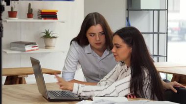 İki çekici iş kadını, modaya uygun, çağdaş bir ofis alanında dizüstü bilgisayar ekranını incelerken derin bir tartışma içindeler. İfadeleri azim ve yaratıcılığı yansıtıyor, dinamik bir ortaklık ortaya koyuyor.