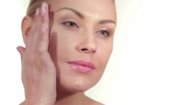 Güzel beyaz bir kadının çarpıcı yakın plan portresi, narin elleri kusursuz tenini el değmemiş beyaz bir fon üzerinde okşuyor. Bu resim doğal güzelliği ve zarafeti yansıtıyor, büyüleyici yeşil gözlerini ve yumuşak, parlak gözlerini gösteriyor.