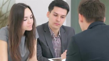 Genç ve çekici bir çift, şık ofis ortamlarıyla çevrili iş analistleriyle odaklanmış bir tartışmaya giriyorlar. İfadeleri, bir tablet üzerinde strateji kurarken azim ve coşkuyu yansıtıyor.