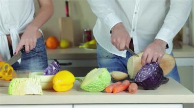 Canlı bir mutfakta, iki genç arkadaş keyifli bir akşam yemeği için havuç ve lahana da dahil olmak üzere renkli sebzeleri dilimliyorlar. Gülümsemeleri mutluluk saçıyor, birlikte taze ve sağlıklı bir yemek yaratırken, yemek pişirmenin sevincini gösteriyorlar.