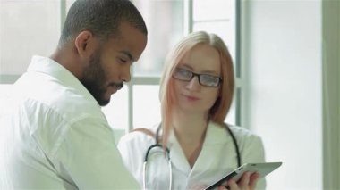 Parlak, modern bir klinikte, odaklanmış bir doktor ve bir hasta zarif bir tablette tıbbi sonuçları incelerken anlamlı bir tartışmaya girişirler. Boynuna steteskop dolamış özenli bir doktor profesyonellik ve özen gösteriyor.