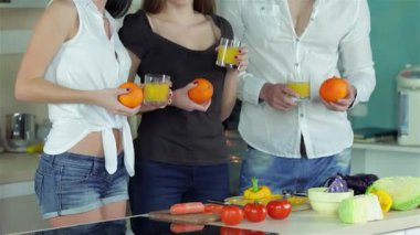 Canlı portakal suyu bardakları tutan üç neşeli arkadaş taze sebzelerle dolu parlak bir mutfakta toplanıyorlar. Kahkahalar, rengarenk bir yemek hazırlarken havayı dolduruyor. Yemek pişirmenin ve arkadaşlığın sevincini sergiliyorlar.