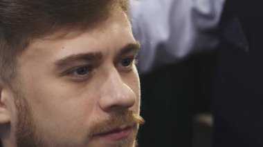 Çarpıcı bir yakın plan, genç ve yakışıklı bir adamın saçını ustalıkla şekillendiren yetenekli bir berber gibi düşünceli bakışlarını yakalıyor. Sahne profesyonelliği ve stili yansıtıyor, canlı bir berber dükkanında tımar sanatını sergiliyor.