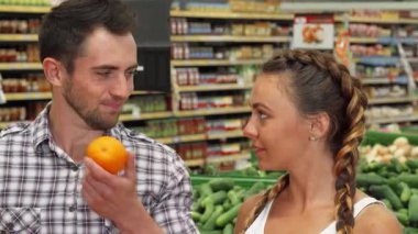Neşeli genç bir çift, canlı bir markette taze portakal aromasını içine çekerek keyifli bir anı paylaşıyor. Yakışıklı adam ve güzel kız arkadaşı etrafları renkli meyvelerle çevrili sağlıklı meyve seçimine dalmış durumdalar.