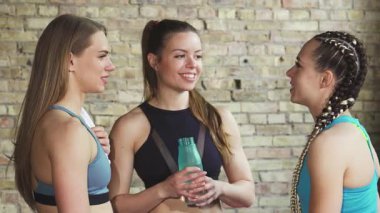 Üç formda kadın spor salonunda neşeli bir anı paylaşıyor canlandırıcı bir egzersizden sonra hareketli bir şekilde sohbet ediyorlar. Canlı spor kıyafetleri ve ışıltılı gülümsemeleri güçlü bir dostluk bağını ve sağlıklı bir yaşam tarzını yansıtıyor.