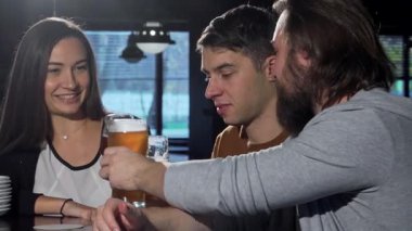 Sakallı bir adam keyifle kadehini kaldırır, arkadaşlarıyla birlikte sıcak bir barda tazeleyici bira içerek kutlama yapar. Sıcak atmosfer ve kahkahalar, gevşemek ve hayatın tadını çıkarmak için mükemmel bir atmosfer yaratıyor.