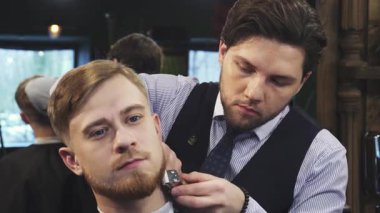 Yetenekli bir berber, sıcak ışıklandırma ve klasik dekorla çevrili kaliteli bir berber dükkanında yakışıklı bir genç adamın sakalını budamaya odaklanır. Bu samimi sahne, kuaförlüğün, berberlerin hassasiyetinin ve müşterinin sanatını yansıtıyor.