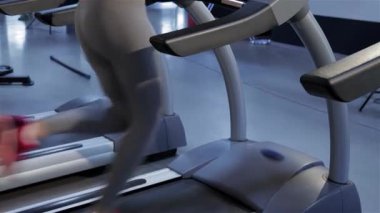 Enerjik zinde bir kadın antrenmanına dalmış modern bir spor salonundaki koşu bandında müzik dinliyor. Bu canlı sahnede zarif, pembe benekli bluzlu ve parlak gri taytlı ince kızıl saçlı biri forma bağlılığını sergiliyor.