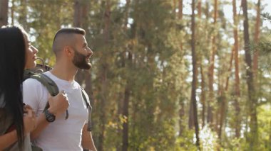 Çekici bir erkek yürüyüşçü canlı yeşil bir ormanın ortasındaki kız arkadaşının yolunu güvenle gösterir. Sırt çantaları omuzlarında gezen çift, güzel kumralın sevgi ve macerayı somutlaştırarak ona baktığı keyifli bir anı paylaşıyor.
