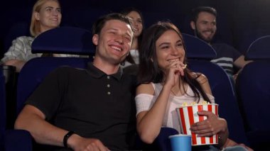 Çekici bir genç adam, bir komedi filmi gösterimi sırasında gülüşlerini paylaşan sevgili sevgilisini kucaklıyor. Etrafları film izleyicileriyle çevriliyken patlamış mısırın ve aşkın özünü somutlaştıran sinematik bir maceranın hoş atmosferinin tadını çıkarıyorlar.