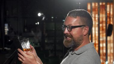 Neşeli sakallı bir adam barda oturmuş arkadaşını beklerken viskinin tadını çıkarıyor. Lokantanın sıcak atmosferi akıllı telefonuna göz atarken heyecanı arttırıyor, gece hayatı boyunca dijital dünyayla bağlantı kuruyor.