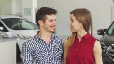 Ellerinde araba anahtarlarıyla, galeride yeni otomobillerini kutlarken heyecan dolu bir çift. Parlak gülümsemeleri ve sevgi dolu kucaklamaları sahipliğin heyecanını ve yeni bir hayata başlamanın sevincini yakalar.