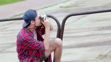 Genç bir adam güneşli bir günde çömelmiş, neşeli arkadaşlarının fotoğraflarını çekiyor, dışarıda birlikte eğleniyorlar ve gülüyorlar. Bu canlı sahne, dostluk ve anıları resim gibi bir ortamda yakalamanın sevincini yansıtıyor.
