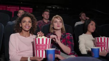 Canlı bir grup genç arkadaş, sıcak bir sinemada, kahkaha ve heyecanı paylaşan bir film karşısında büyülenir. Ellerinde patlamış mısır ve yanlarında içeceklerle, neşeli atmosfer kendilerini sinematik deneyime daldırırken neşe saçıyor.