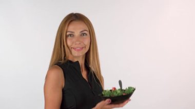 Kameraya uzun, dalgalı saçları olan ışıl ışıl bir sporcu kadın canlı bir tas taze salata tutarken kendini şımartmaya hazır. Gösterişli spor kıyafetleri içinde, sağlıklı ve zinde görünüyor, besleyici yiyeceklerin güzelliğini gösteriyor.