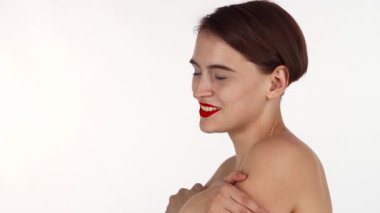 Göz kamaştırıcı kırmızı dudakları olan ışıl ışıl bir kadın kendini kucaklarken neşe içinde güler, kendine güven ve şehvet saçar. Bu kırpılmış çekim onun güzel yüz hatlarını ve teninin yumuşak parıltısını yakalar, izleyicileri güzelliği ve kendini sevmeyi kutlamaya davet eder.