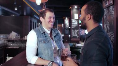 Biri kot yelekli, diğeri koyu renk gömlekli iki neşeli arkadaş coşkulu bir barda kutlama için kadehlerini kaldırıyorlar. Titreşimli atmosfer kahkahalarla ve arkadaşlıklarla dolu. İçkinin tadını çıkarıyorlar.