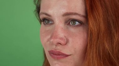 Canlı kızıl saçlı, büyüleyici bir genç kadın portresi. Düşünceli ifadesi kameralara bakarken yer değiştiriyor. Canlı yeşil renkli bir arka plana sahip, güzelliği güven ve kadınlık yayıyor, izleyicileri davet ediyor.