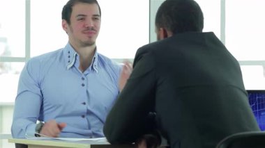 Güçlü bir tokalaşma, çağdaş bir ofiste şık bir masada oturan iki başarılı iş adamı arasındaki anlaşma anını yakalar. Atmosfer hırs ve işbirliği ile dolu.