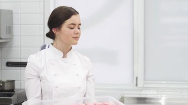 Neşeli genç bir kadın, yetenekli bir pasta şefi, parlak bir ticari mutfakta güzelce işlenmiş badem kurabiyeleriyle dolu bir tepsiyi elinde tutarken gururla ışıldıyor. Pişirmeye olan tutkusu herkesi bu tatlı şeylere davet ediyor.