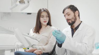 Kendine güvenen genç bir kadın modern bir diş kliniğinde oturmuş, yetenekli dişçisini dikkatle dinliyor ve tedavi seçeneklerini anlatıyor. Parlak ve steril ortam, sağlıklı dişlerin korunmasında profesyonelliği ve özeni vurguluyor.